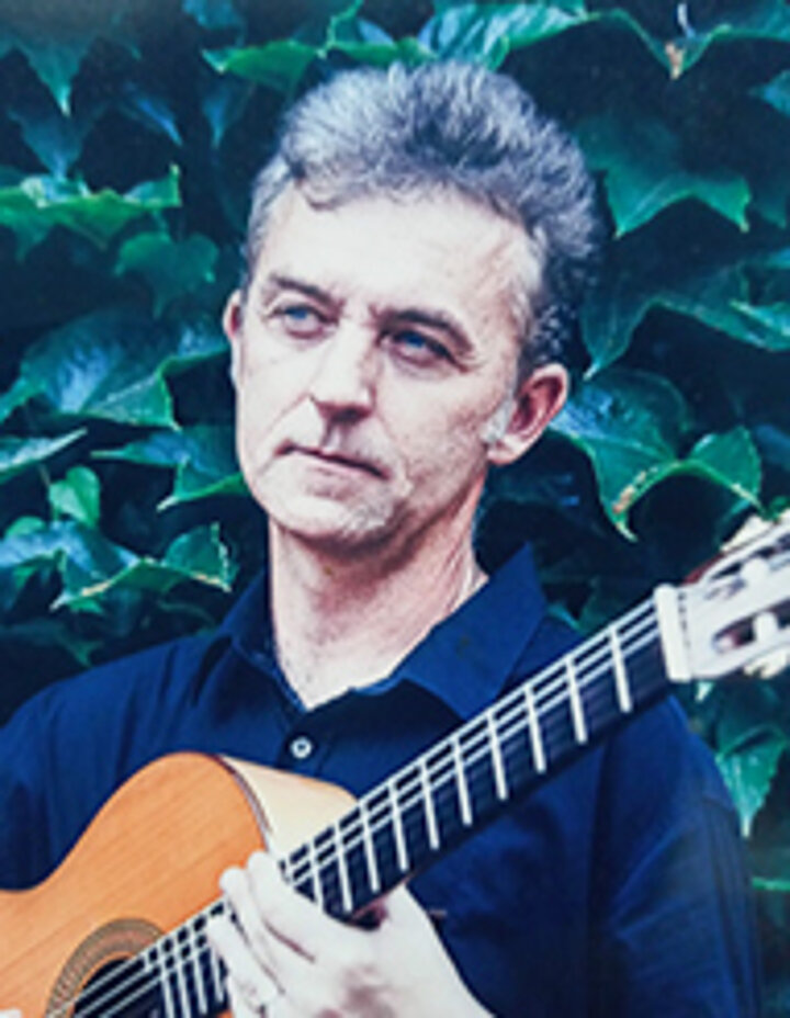 Portretowe zdjęcie mężczyzny w średnim wieku, trzymającego gitarę klasyczną.