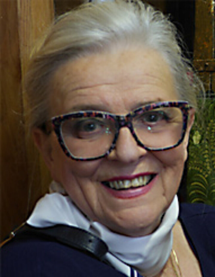 Portretowe zdjęcie dojrzałej, uśmiechniętej kobiety, noszącej okulary z wielokolorowymi oprawkami.
